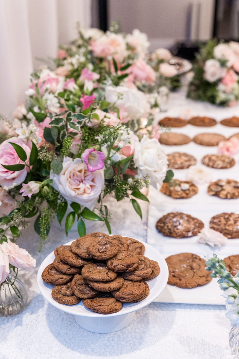 Magnolia cookies on a white dessert table with pink and white flowers at a catered event