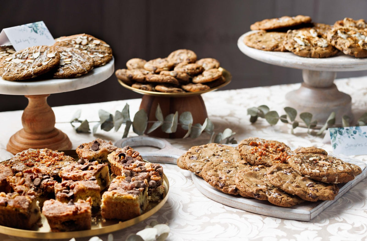 Magnolia cookies and Grandma BB's coffee cake on cake stands, including Earl Grey fig, salted brown butter chocolate chip and s'mores cookies